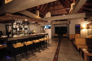 Un espace bar doté d’un plafond haut, de poutres en bois et d’un comptoir avec des tabourets.