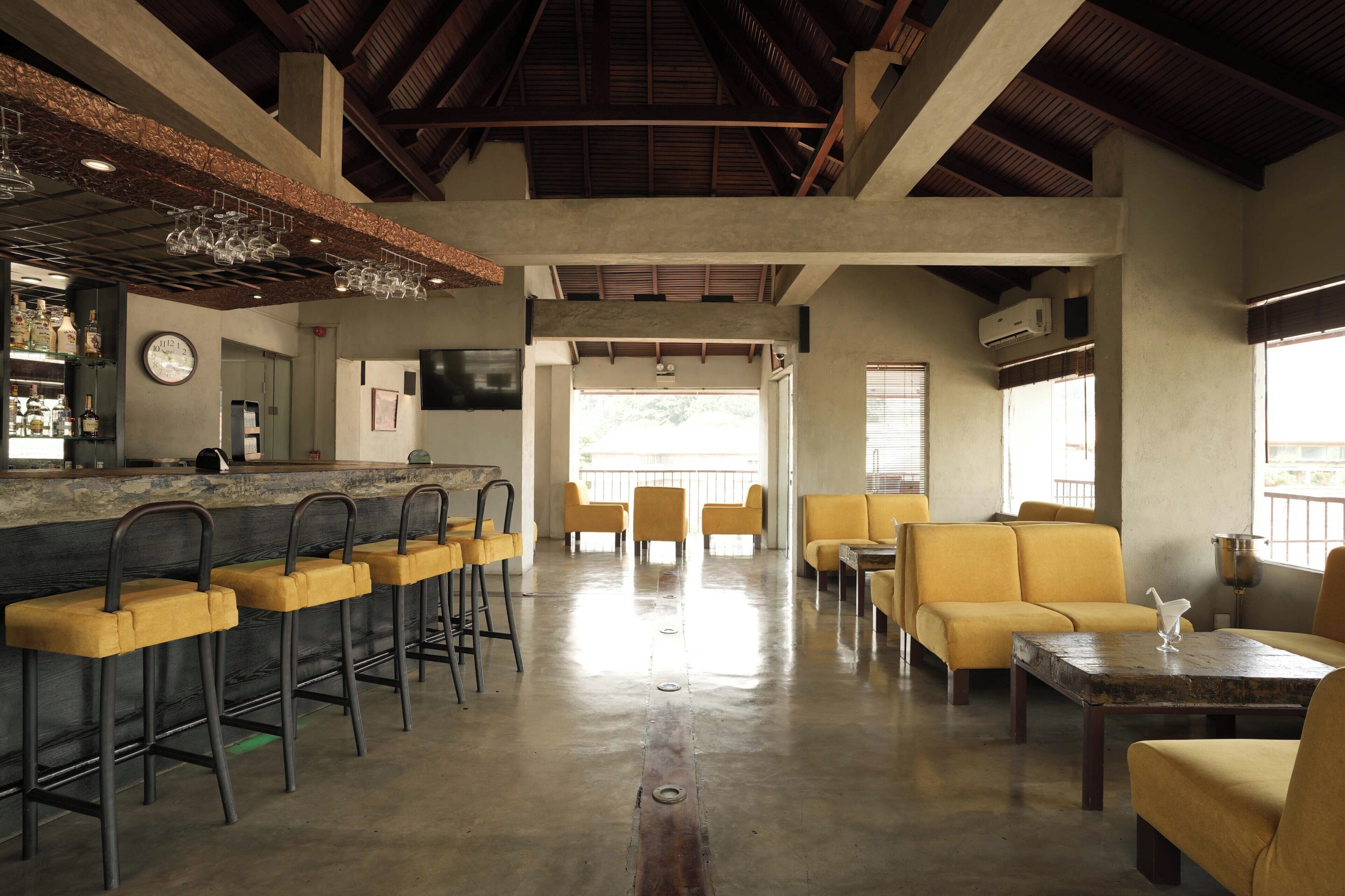 Zona de bar con taburetes, una barra y un área de asientos con sofás amarillos y una mesa.