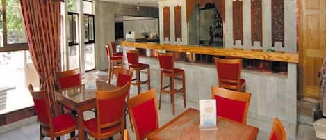 Un restaurant avec des tables en bois et des chaises rouges, un coin bar et des panneaux décoratifs sur les murs.