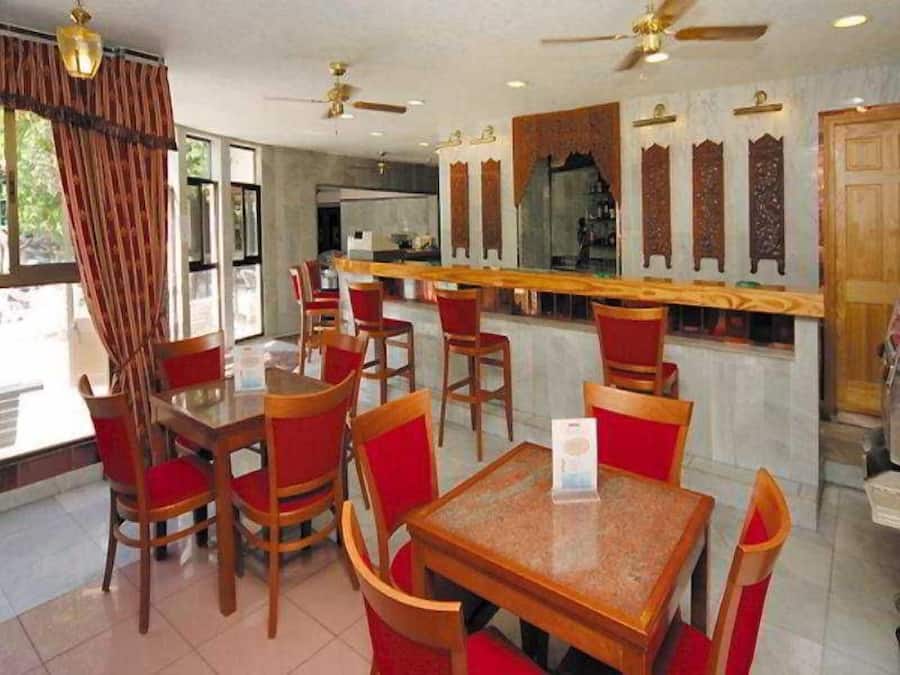 Un restaurante con mesas de madera, sillas rojas, una zona de bar y paneles decorativos en las paredes.
