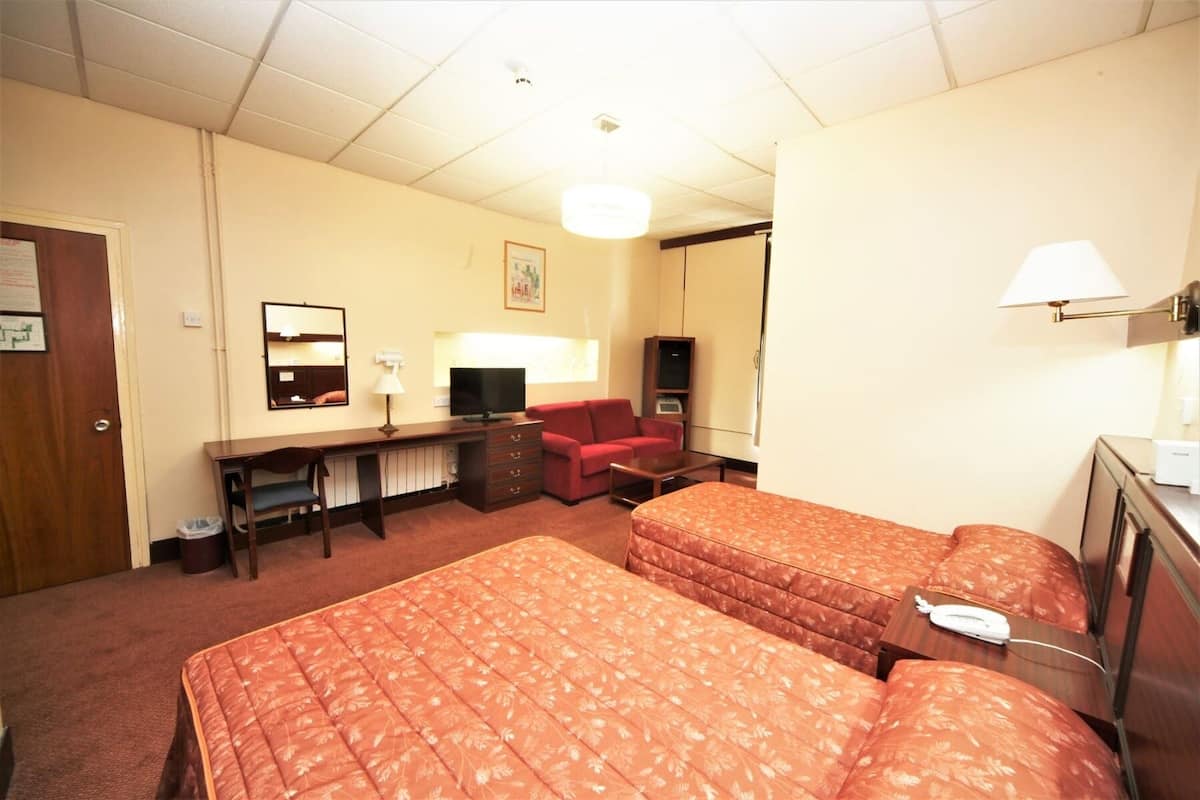 A hotel room with two beds, a desk, a television, a red sofa, and a lamp.