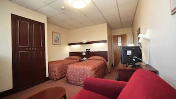 A hotel room with two beds, a desk with a computer, a TV, and a red couch.