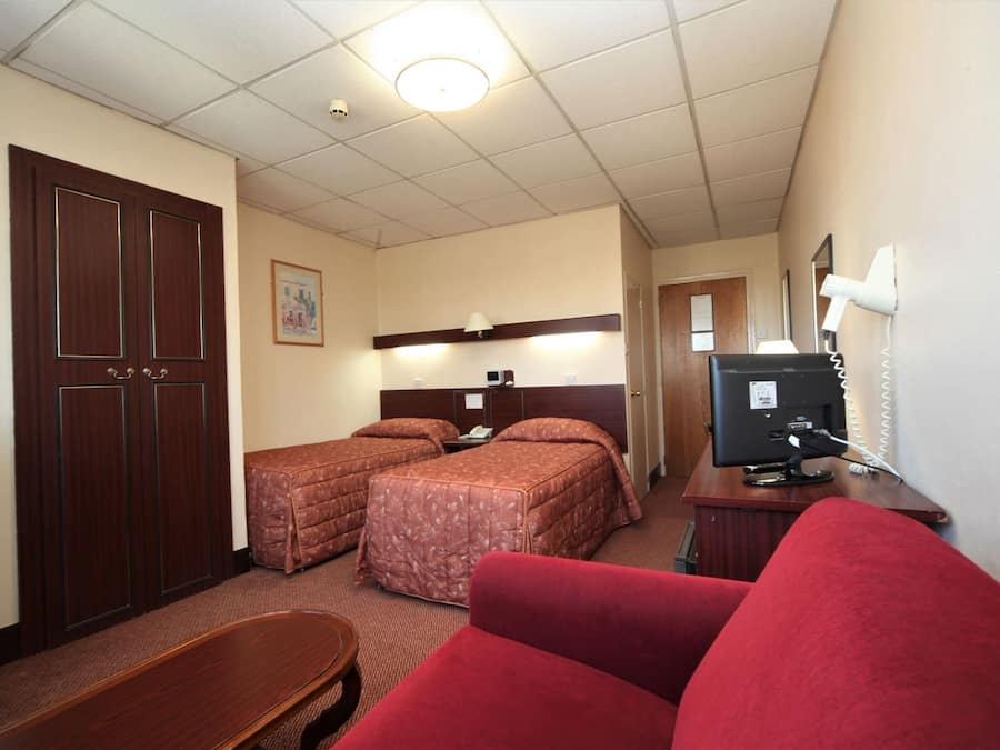 Una habitación de hotel con dos camas, un escritorio con computadora, un televisor y un sofá rojo.