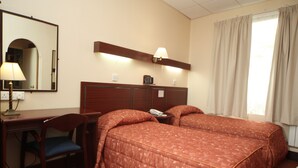 A hotel room with two beds, a desk with a chair, a mirror, a lamp, and a window with curtains. - Bristol (Gibraltar)
