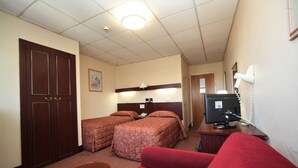 A hotel room with two beds, a desk with a computer, a TV, and a red couch. - Bristol (Gibraltar)