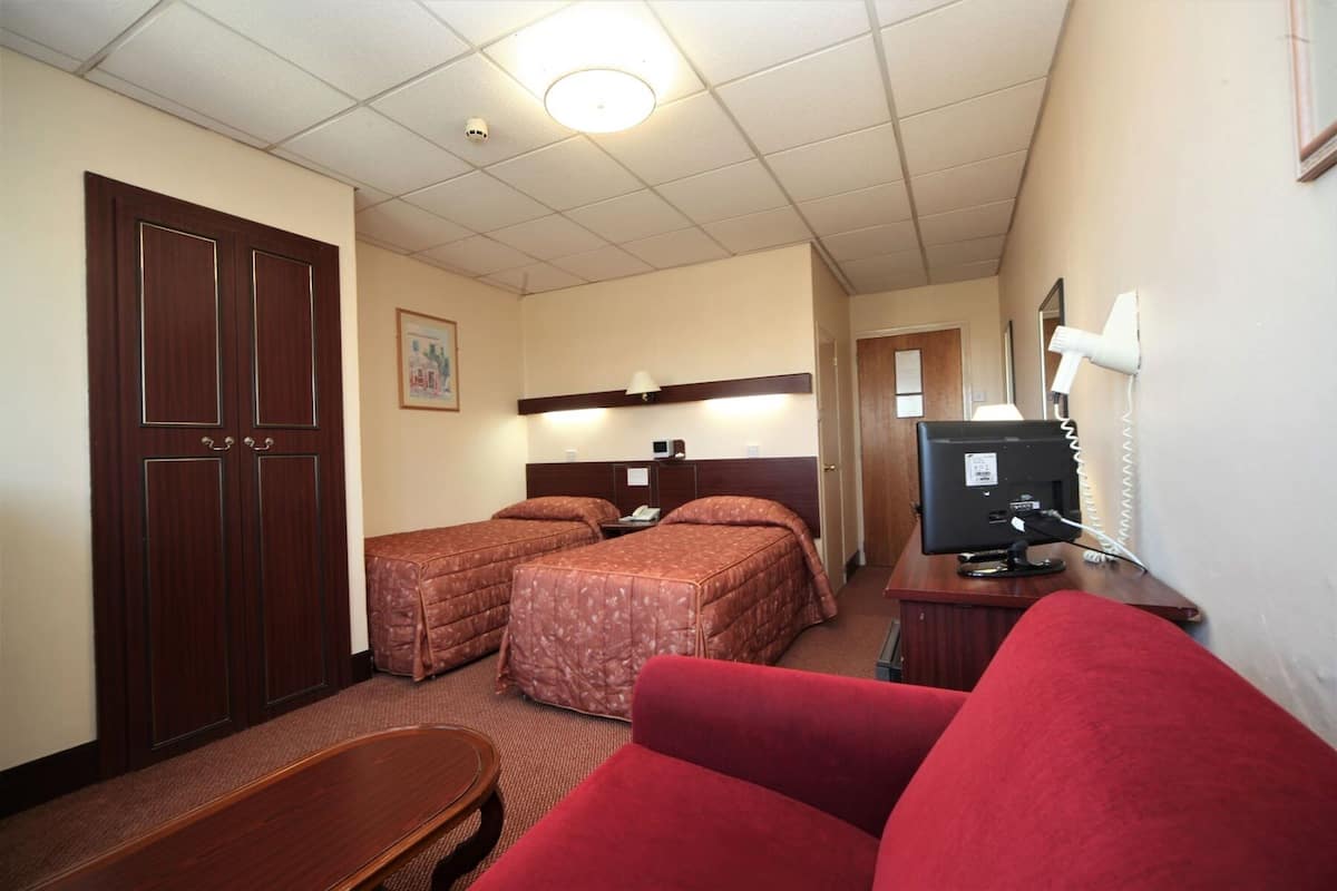 A hotel room with two beds, a desk with a computer, a TV, and a red couch.