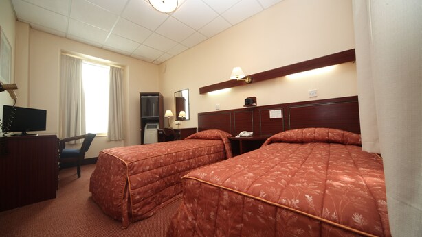 A hotel room with two beds, a desk, a chair, a television, and a window with curtains. - Bristol (Gibraltar)