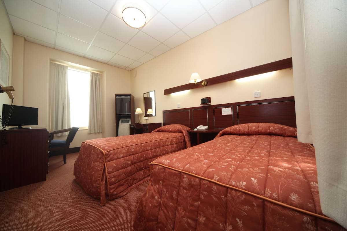 A hotel room with two beds, a desk with a computer, a chair, a TV, and a window with curtains.