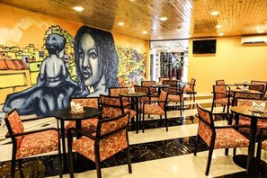 Un restaurante con un mural en la pared, varias mesas y sillas, y un techo de madera.