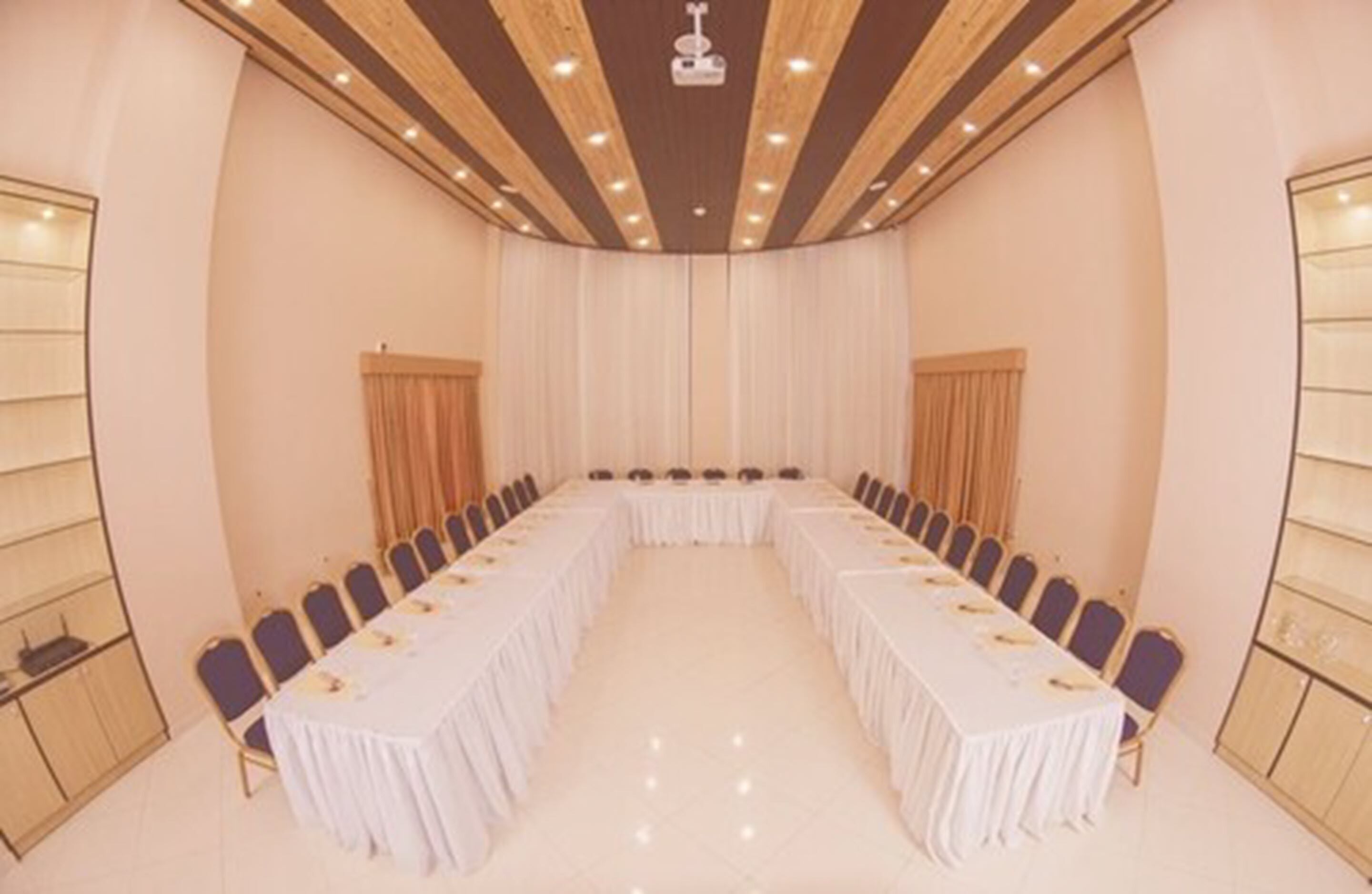 A conference room with a long table, chairs, and a white curtain backdrop.