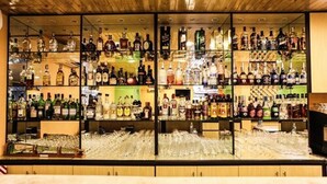 Zona de bar con estantes llenos de botellas de licores y una variedad de vasos.