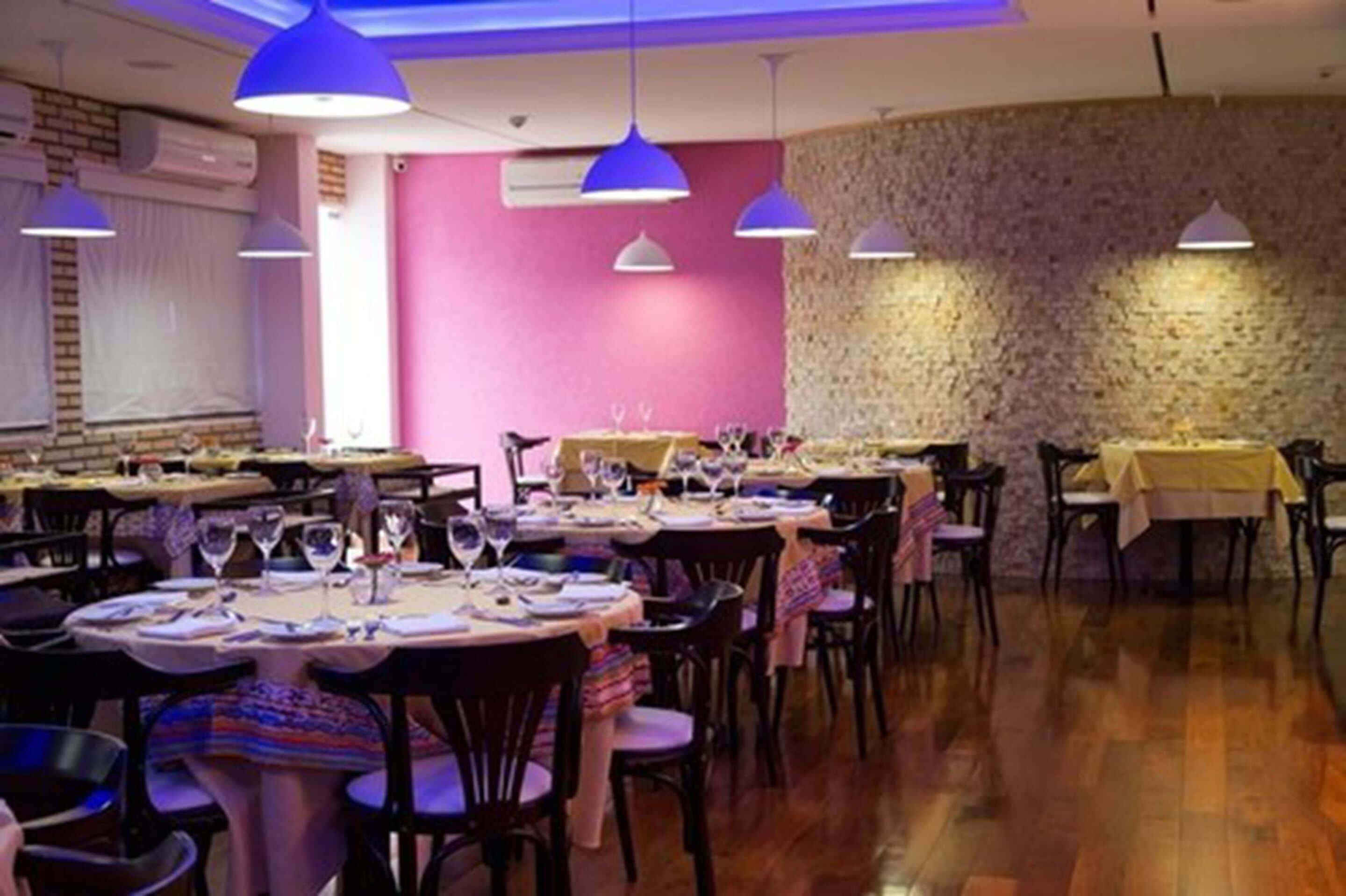 A restaurant with multiple tables set for dining, featuring pendant lighting and a brick wall backdrop.