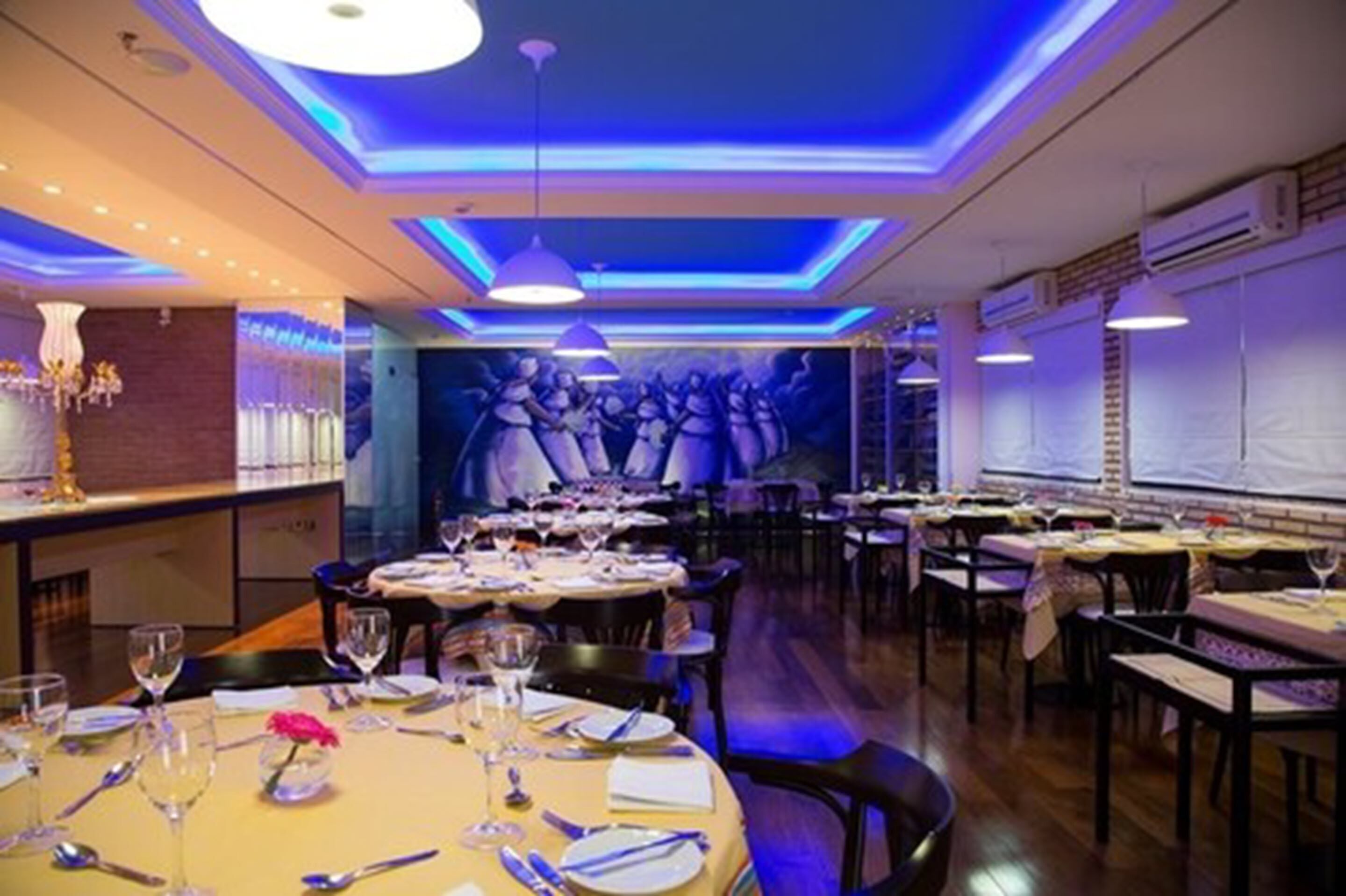 Un restaurante con varias mesas, iluminación azul tenue y un mural en la pared trasera.