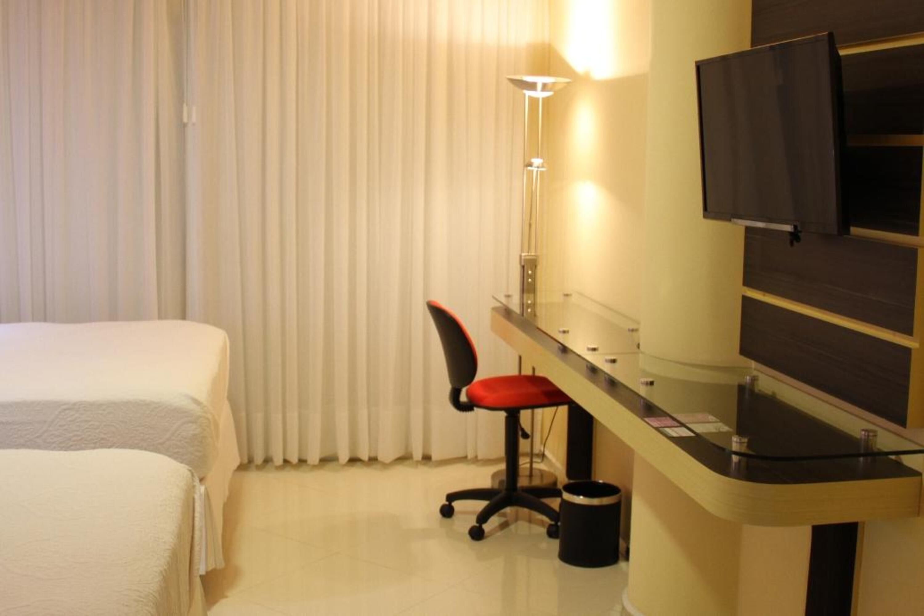 Habitación de hotel con dos camas, un escritorio con silla, un televisor y una lámpara.