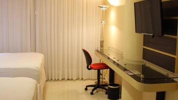 Habitación de hotel con dos camas, un escritorio con silla, un televisor y una lámpara.