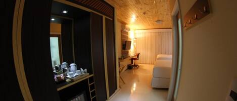 A hotel room with a wooden ceiling, a large mirror, a bed, a desk with a chair, and a small kitchenette area.