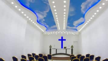 Interior de iglesia con un crucifijo, hileras de sillas y un techo con diseño de nubes.