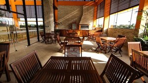 Un comedor interior con mesas y sillas de madera, ventanas amplias y una pared de piedra.