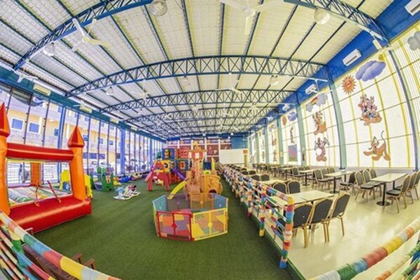 Un amplio espacio interior para juegos con techo alto, estructuras de recreación y mesas y sillas dispuestas para comer.