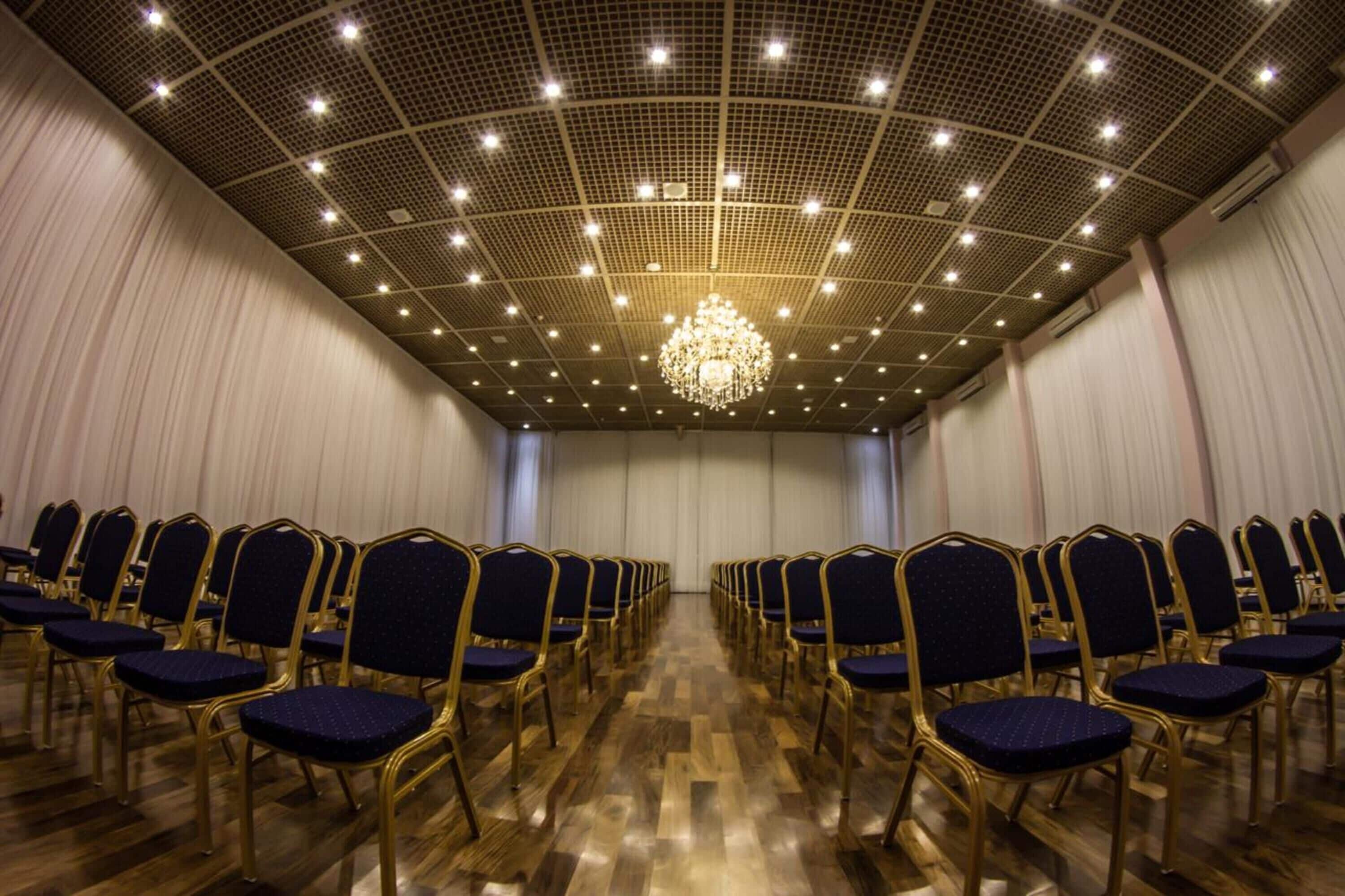 A conference room with rows of blue chairs and a chandelier.