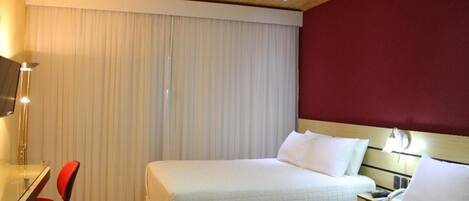 Habitación de hotel con dos camas, un escritorio con silla, televisión y ventana con cortinas.
