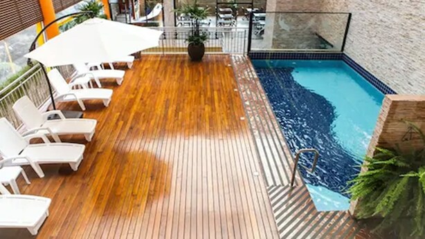 Una terraza de madera con sillones blancos y una piscina.