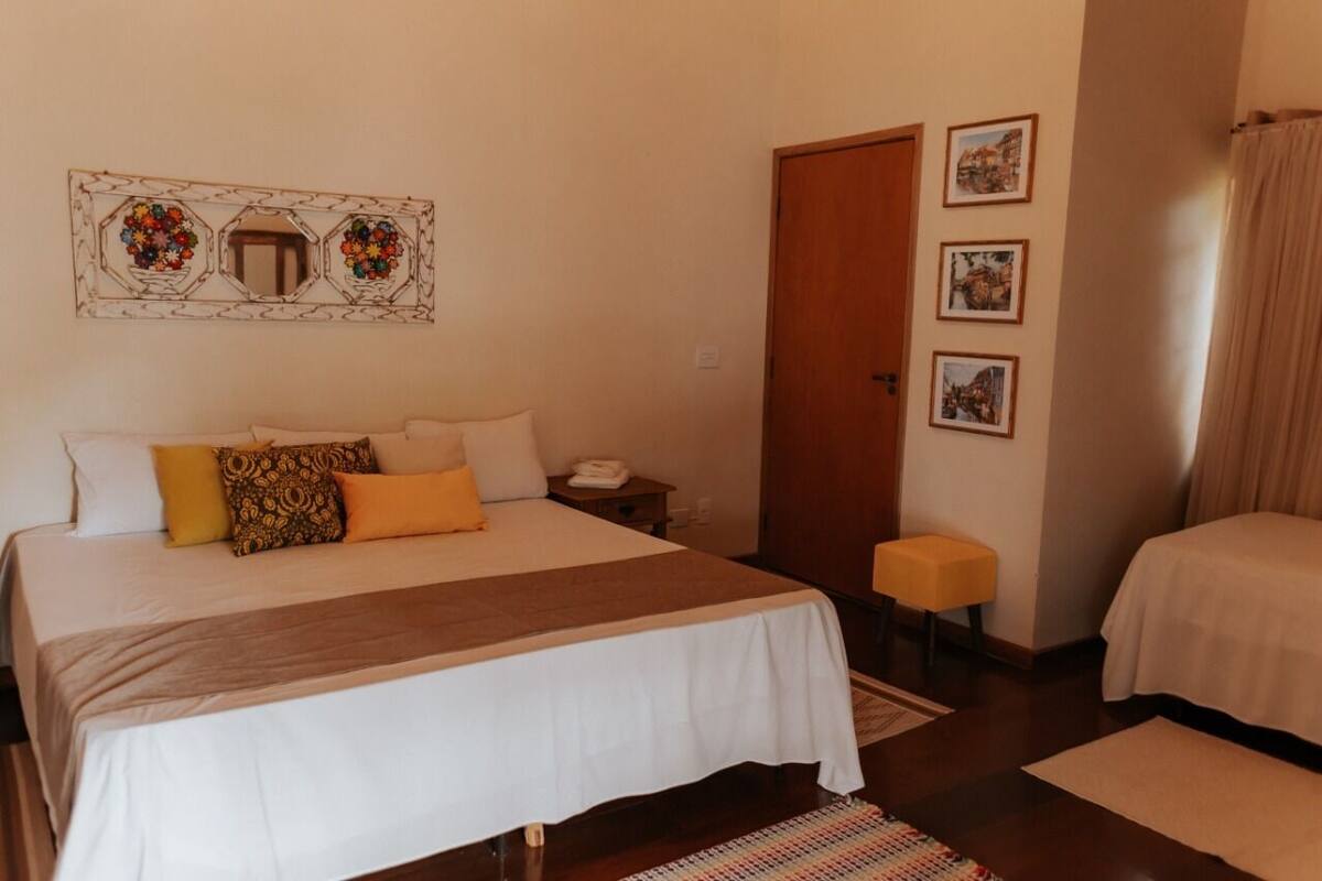 Una habitación de hotel con una cama grande, una mesita de noche con un teléfono, un taburete pequeño y una puerta.