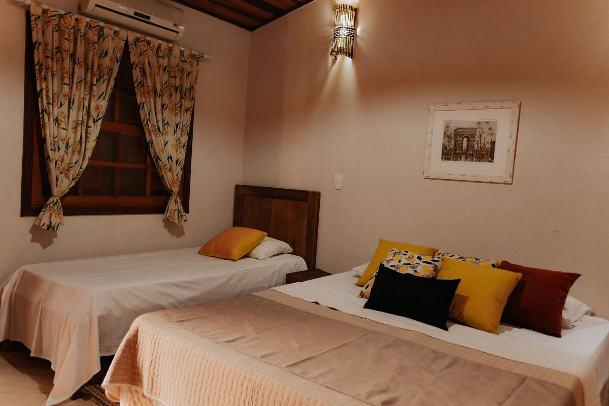 Un dormitorio con dos camas individuales, cabecero de madera, un cuadro en la pared y una ventana con cortinas florales.