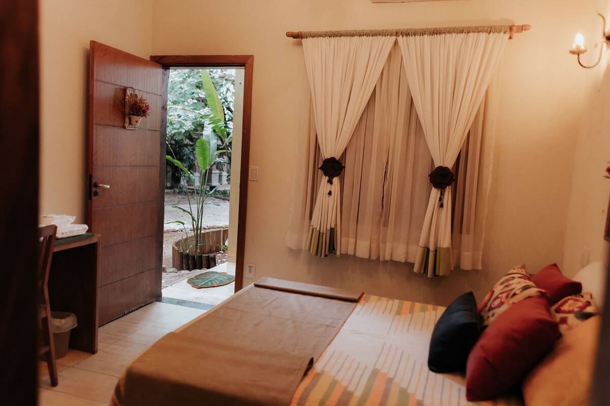 Un dormitorio con cama, escritorio y puerta que da a un espacio exterior con plantas.