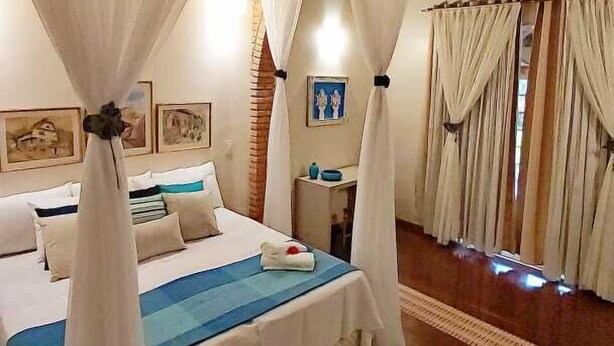 Een slaapkamer met een groot bed, witte gordijnen en een houten plafond.