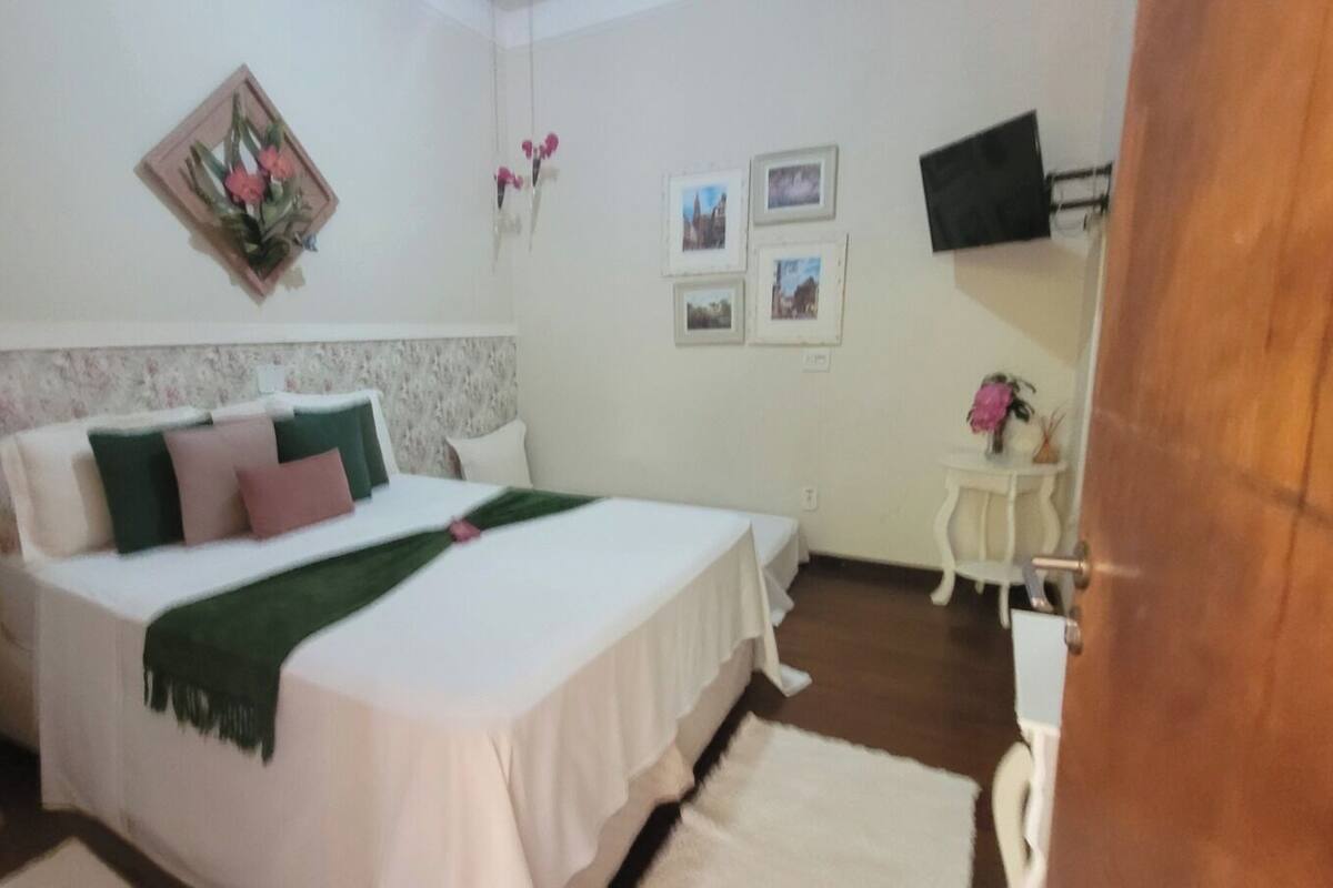 Un dormitorio con cama, cómoda, mesita de noche, televisor y una pequeña mesa con una silla.