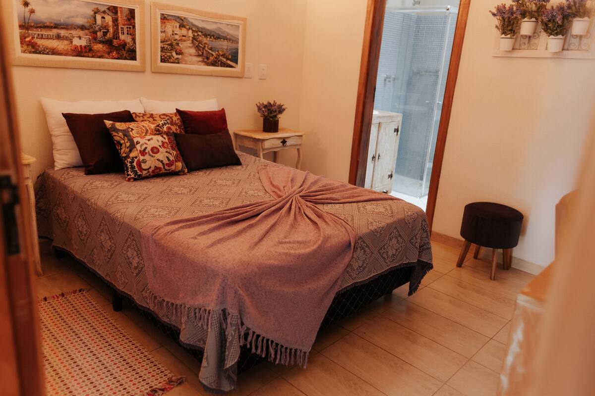 Un dormitorio con cama, mesita de noche, una pequeña mesa y una planta en maceta.