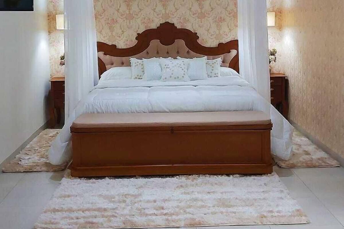 Un dormitorio con una cama grande, dosel, dos mesitas de noche con lámparas, papel tapiz floral y suelo de baldosas.