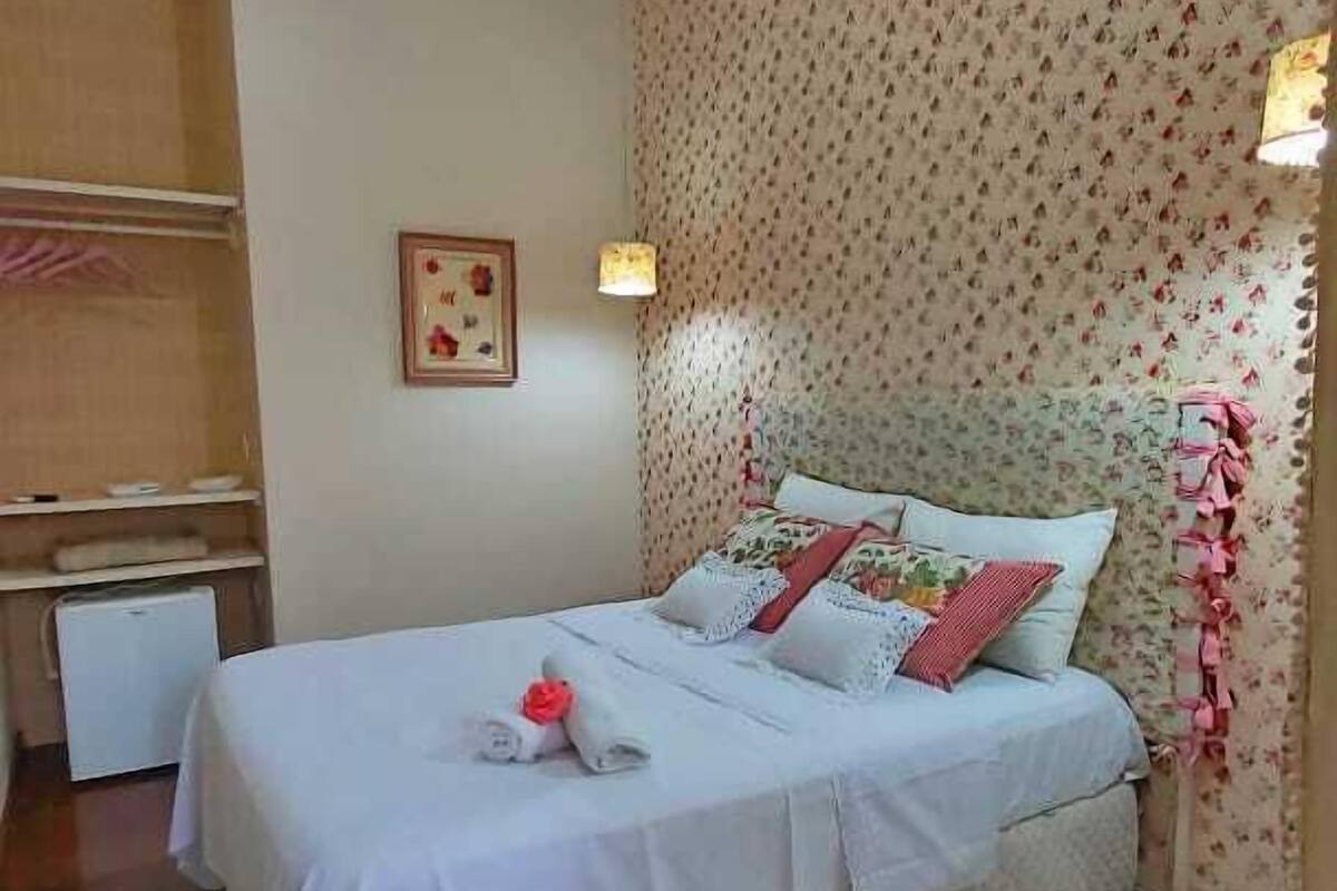 Un dormitorio con cama, mesita de noche, cómoda y pared con papel tapiz floral.
