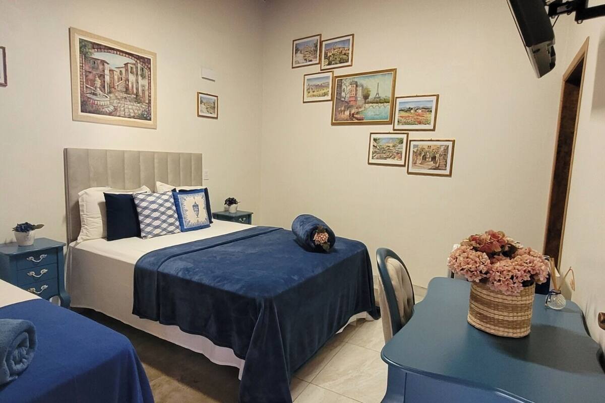Habitación de hotel con dos camas, una cama grande con cabecera, un escritorio con silla y una pared decorada con cuadros.