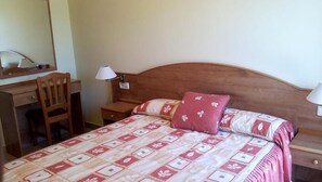 Un dormitorio con cama, escritorio, silla y dos lámparas de noche.