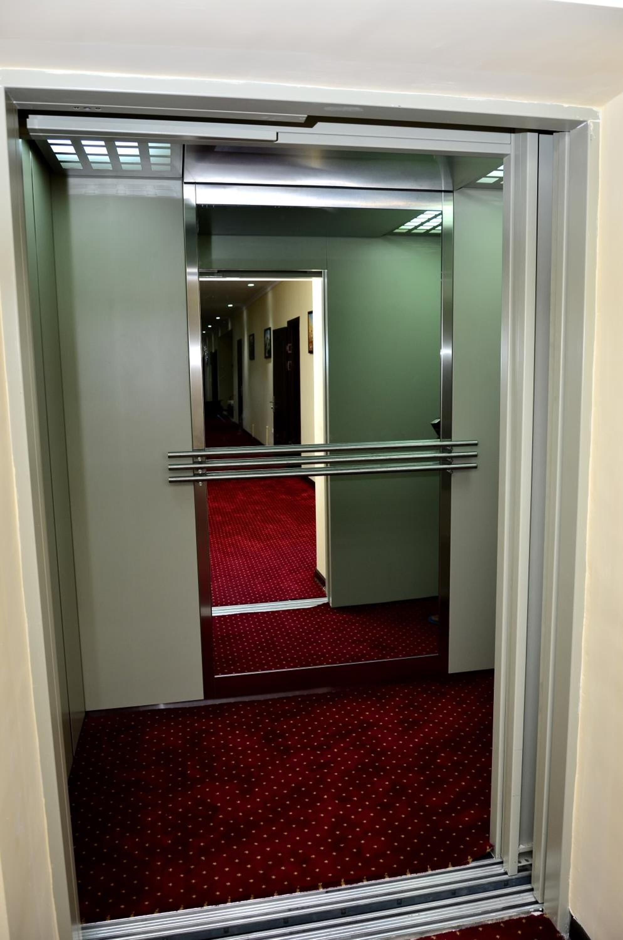 Ascensor de hotel con interior alfombrado en rojo y barandillas metálicas.