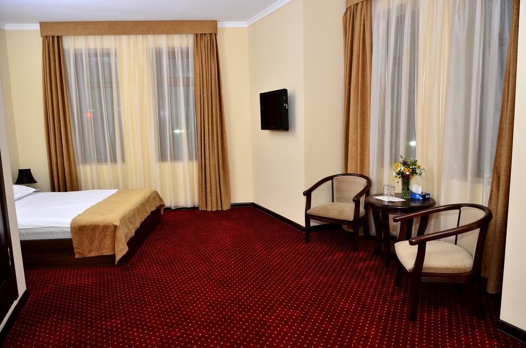 A hotel room with a bed, a small table with a chair, and a TV on the wall.
