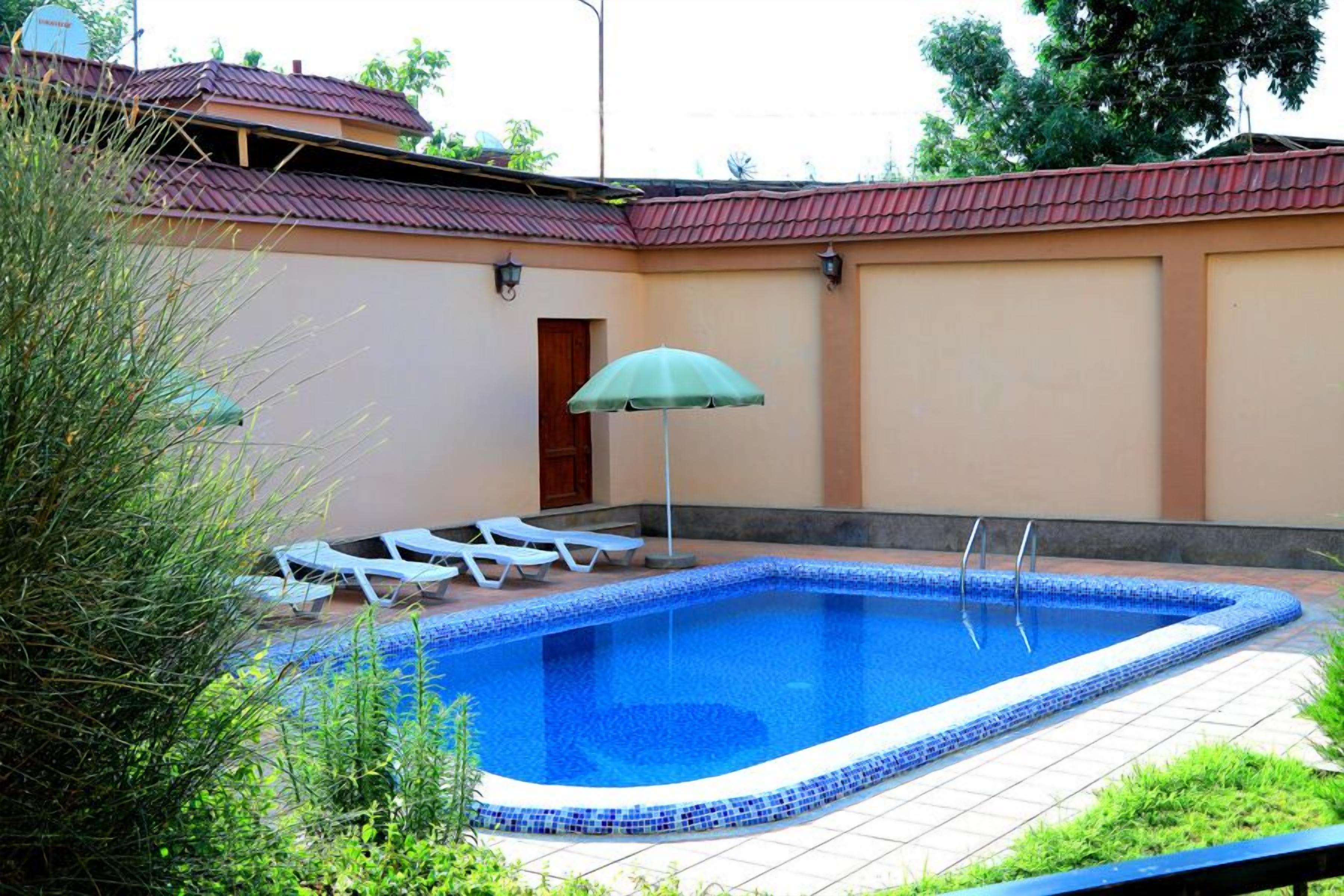 A rectangular swimming pool with a tiled edge, surrounded by a tiled deck. There are lounge chairs and a single umbrella.