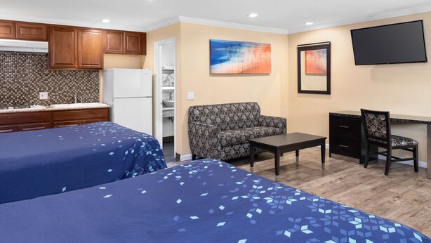 A hotel room with two beds, a kitchenette, a sofa, a desk, and a TV.