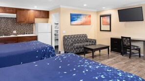 A hotel room with two beds, a kitchenette, a sofa, a desk, and a TV. - Scandia Motel (Carlsbad)
