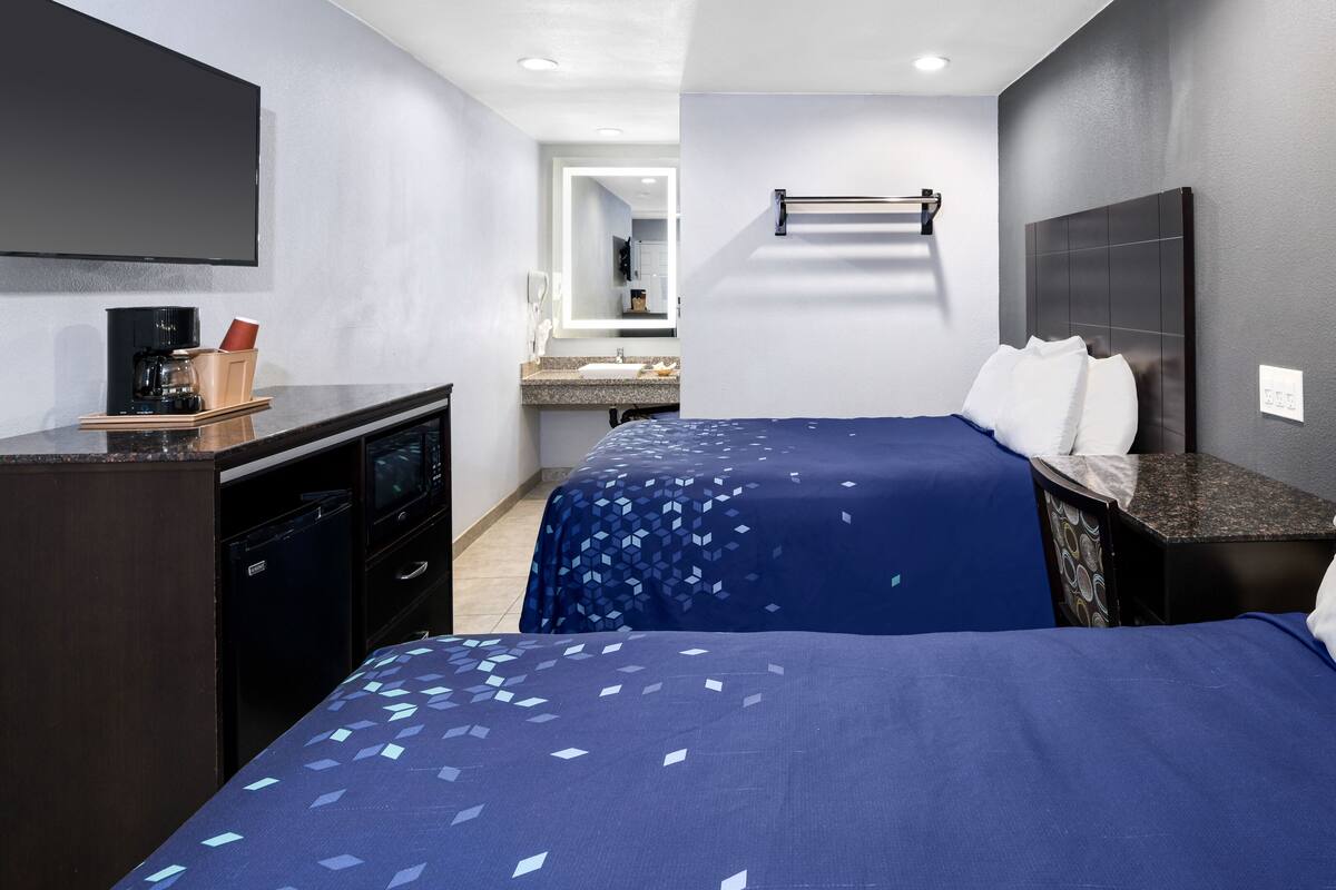 A hotel room with a bed, bedside table, and a desk with a coffee maker.