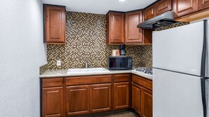 A compact kitchen with wooden cabinets, a white refrigerator, a microwave, and a gas stove.