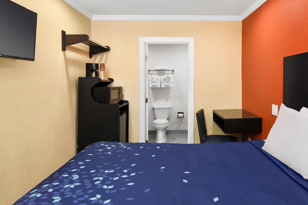 A hotel room with a bed, a desk, a TV, and a toilet.