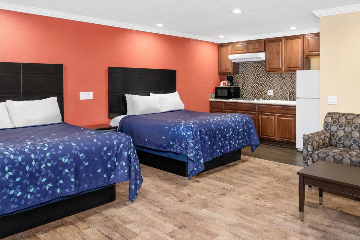 A hotel room with two beds, a kitchenette, and a sofa.