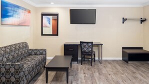 A living room with a sofa, a desk, a chair, and a TV mounted on the wall.