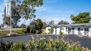 A motel with a signboard, a parking lot, and surrounding greenery.