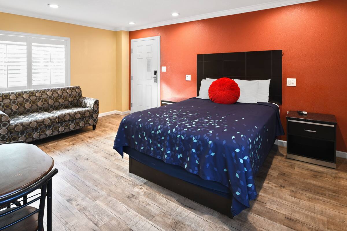 A bedroom with a bed, a nightstand, a chair, and a sofa.