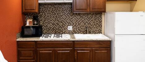 A compact kitchen with wooden cabinets, a microwave, a stove, and a refrigerator.