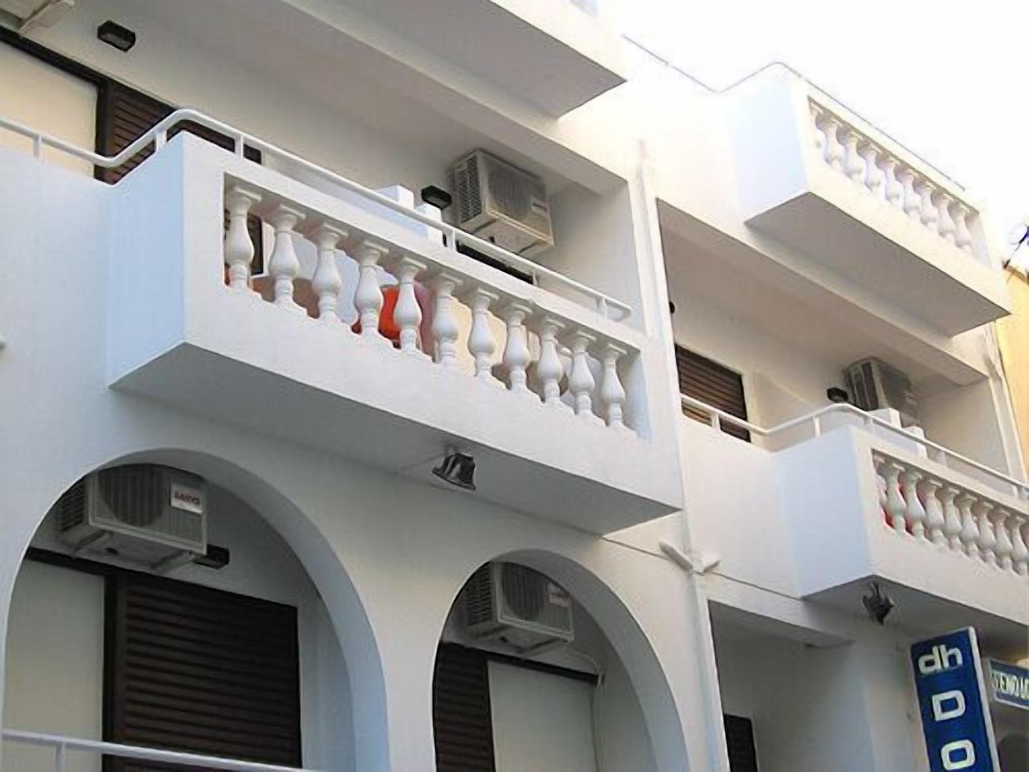A multi-story building with white balconies, air conditioning units, and a blue sign with text.